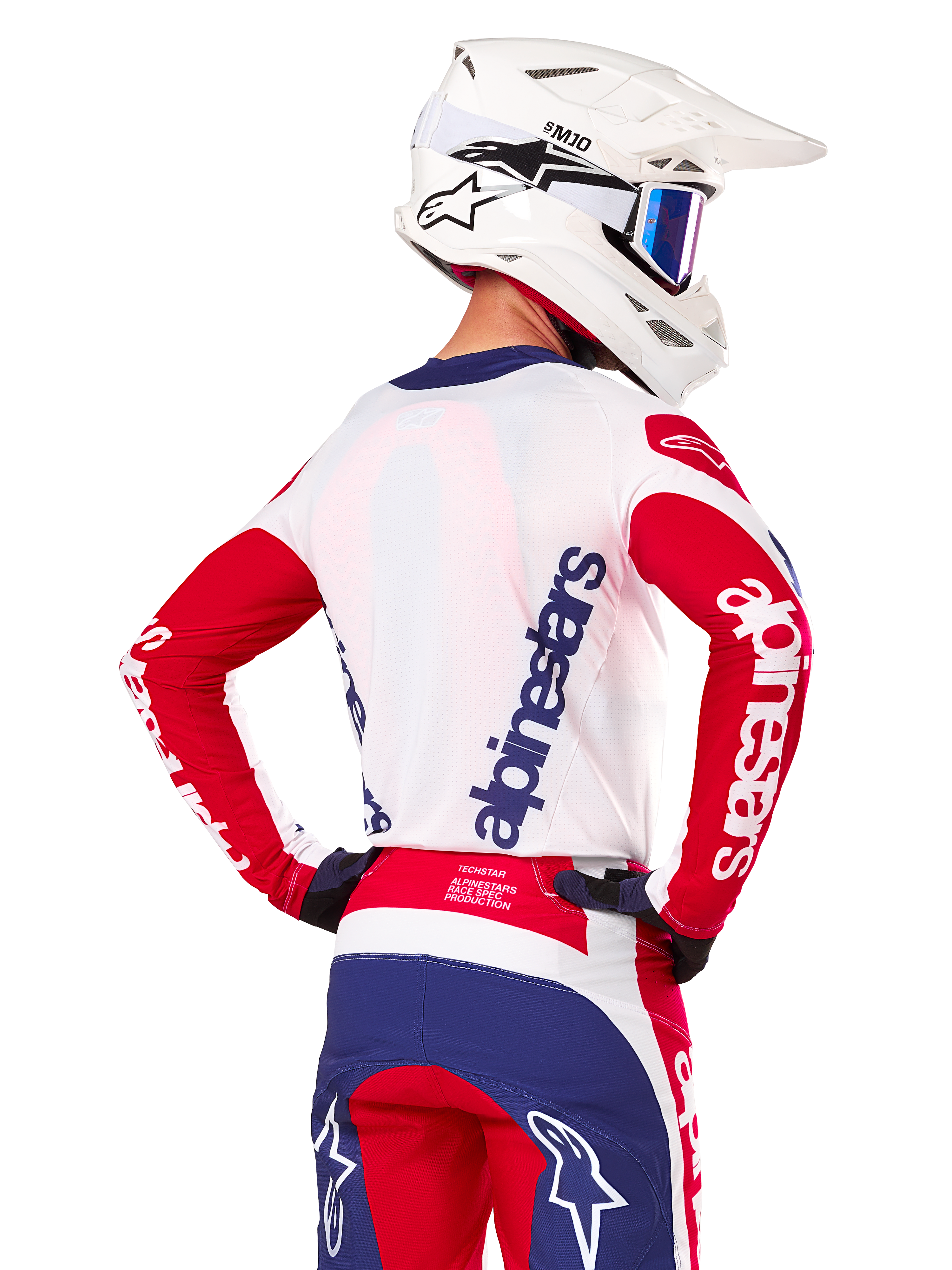 Alpinestars Limited Edition Techstar Fortitude Jersey, Motocross-Trikot, Hellrot, Weiß und Blau, Rückansicht eines Fahrers mit weißem Helm und passender Ausrüstung, markante Alpinestars-Logos auf dem Rücken und den Ärmeln, entwickelt für Hochleistungs-Offroad-Rennsport