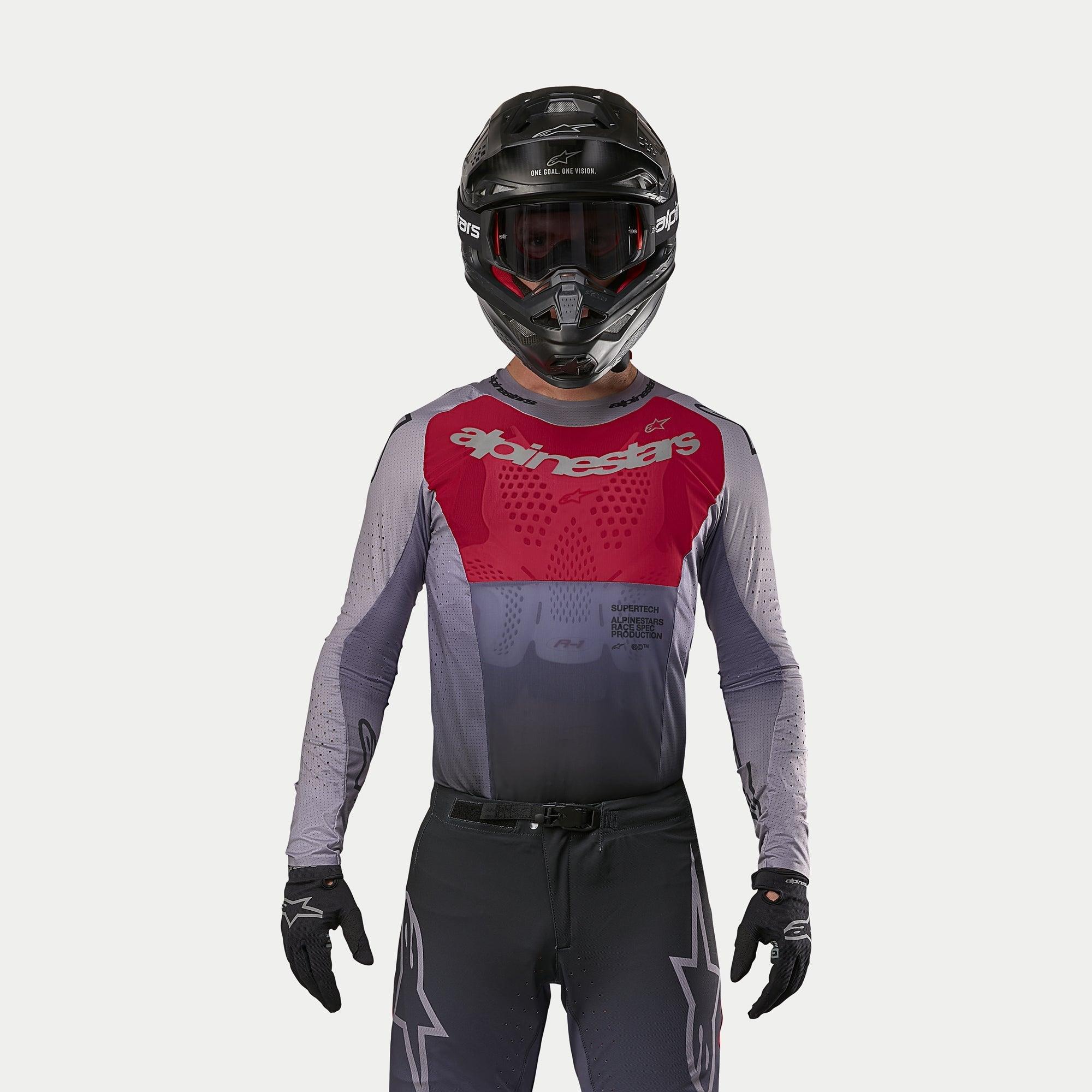 Motocross-Fahrer im Alpinestars 2024 Supertech Dade Jersey in Iron Red Berry, mit rotem Brustbereich und grauen Ärmeln mit silbernem Branding, getragen mit passender Hose, einem schwarzen Helm und schwarzen Handschuhen, professionelle Offroad-Rennausrüstung