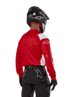 Motocross rider seen from the back wearing the Alpinestars Techdura Jersey in Bright Red with white panels, paired with black off-road pants, a black helmet, and black gloves, coordinated gear for enduro and motocross riding.