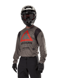 Alpinestars Techdura Jersey, Motocross Off-road Jersey, Falcon Brown with Red Triangle and black branding, worn with black pants, black and white helmet, and black gloves