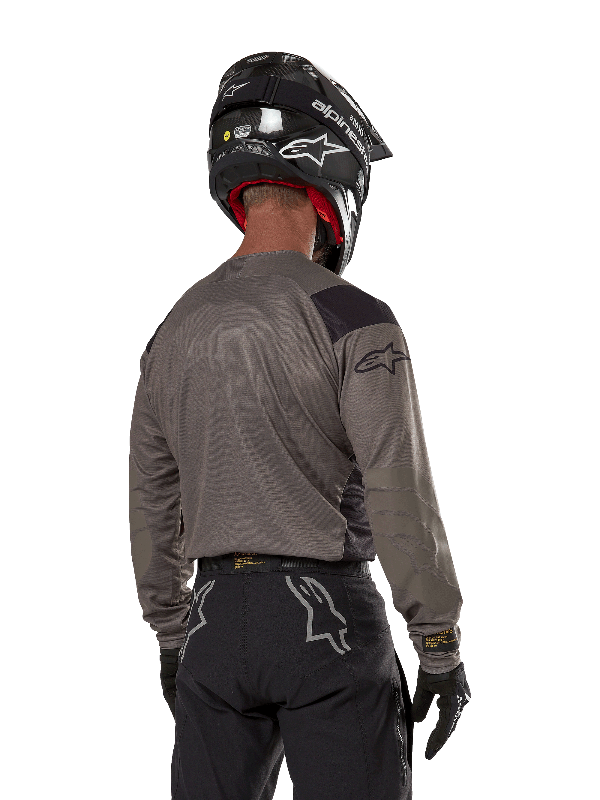 Motocross rider from the back wearing the Alpinestars Techdura Jersey in Falcon Brown, paired with black off-road pants and a black helmet, featuring a modern graphic design and elongated rear for enduro riding