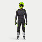 Motocross rider wearing complete racing gear, 2024 Techstar Rantera Jersey in Black Navy and Yellow Fluo, matching abstract print pants, bright fluo yellow helmet, white and black boots, coordinated outfit for off-road racing