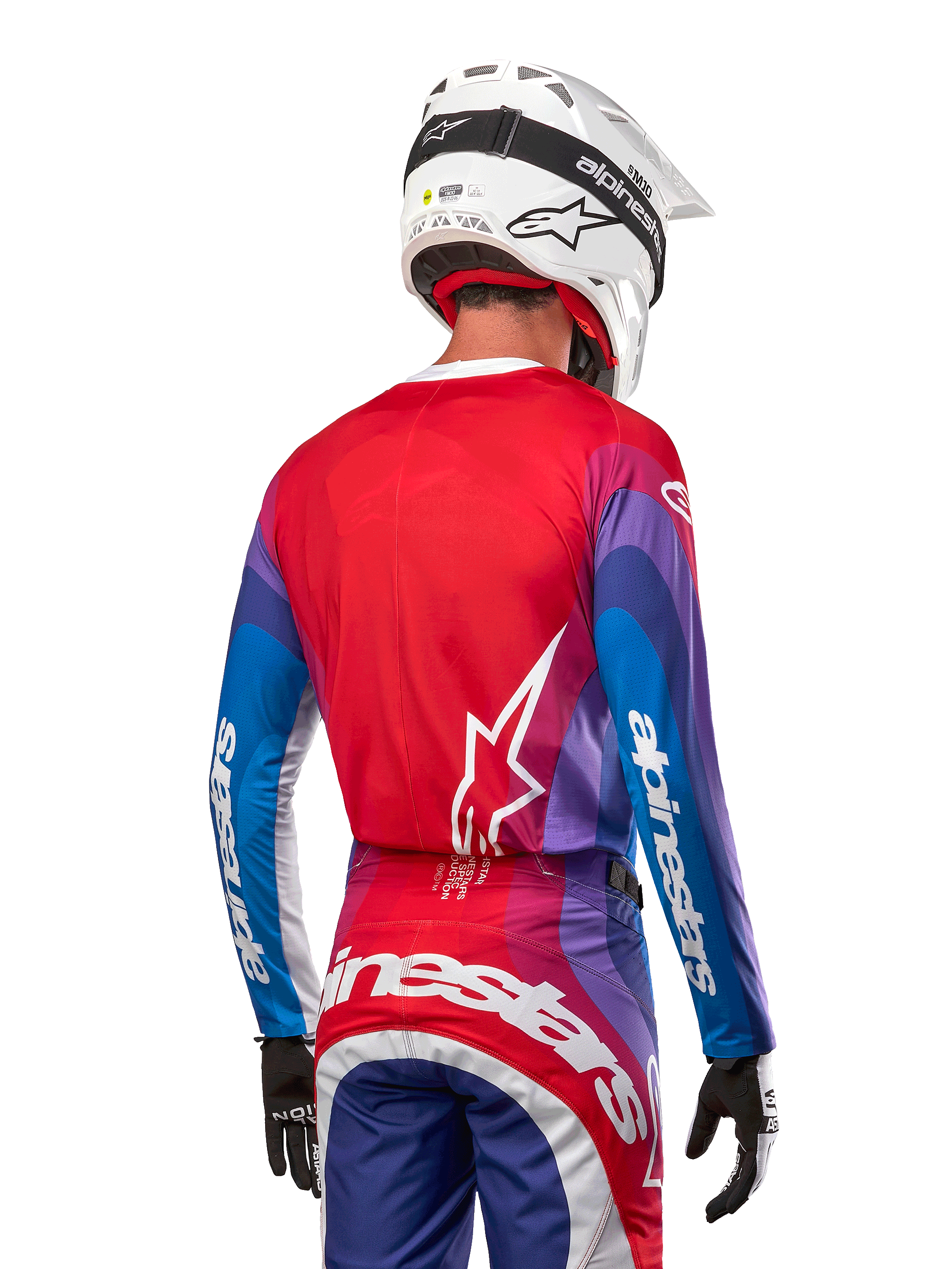 Motocross rider from behind wearing Alpinestars 2024 Techstar Pneuma Jersey in Blue Mars Red White, featuring a red back with white star logo, blue and purple sleeves with white branding, coordinated with matching pants and a white helmet for off-road racing.