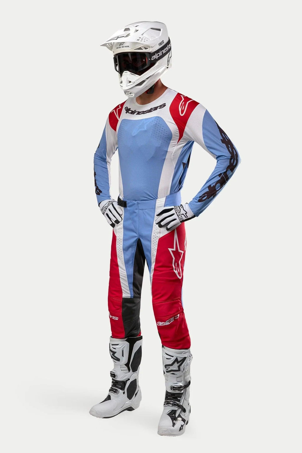 Motocross-Fahrer in kompletter Rennausrüstung mit dem Alpinestars 2024 Techstar Ocuri Trikot in Hellblau, Marsrot und Weiß, passender Hose, weißem Helm mit Schutzbrille, weißen Stiefeln und weiß-schwarzen Handschuhen.