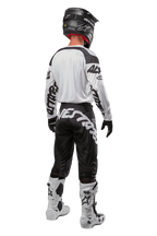 Alpinestars 2024 Racer Hana Trikot, Rückansicht eines Motocross-Fahrers, Weiß und Schwarz, weißes Trikot mit schwarzen Grafiken an den Ärmeln, kombiniert mit einer schwarzen Hose mit weißem Alpinestars-Schriftzug am Gesäß, schwarzer Helm und weiß-schwarze Stiefel, abgestimmte Offroad-Rennausrüstung