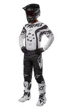 Motocross-Fahrer in kompletter Ausrüstung mit dem Alpinestars 2024 Racer Hana Jersey in Weiß und Schwarz, schwarze Motocross-Hose mit weißen Logos, schwarzer Helm, weiß-schwarze Racing-Stiefel und schwarze Handschuhe, professionelles Offroad-Rennoutfit