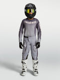 Alpinestars Fluid Jugend-Trikot Amber und Gear Set 2027, grau-sandfarbene Motocross-Kombi, schwarzer Helm, weiße Stiefel.