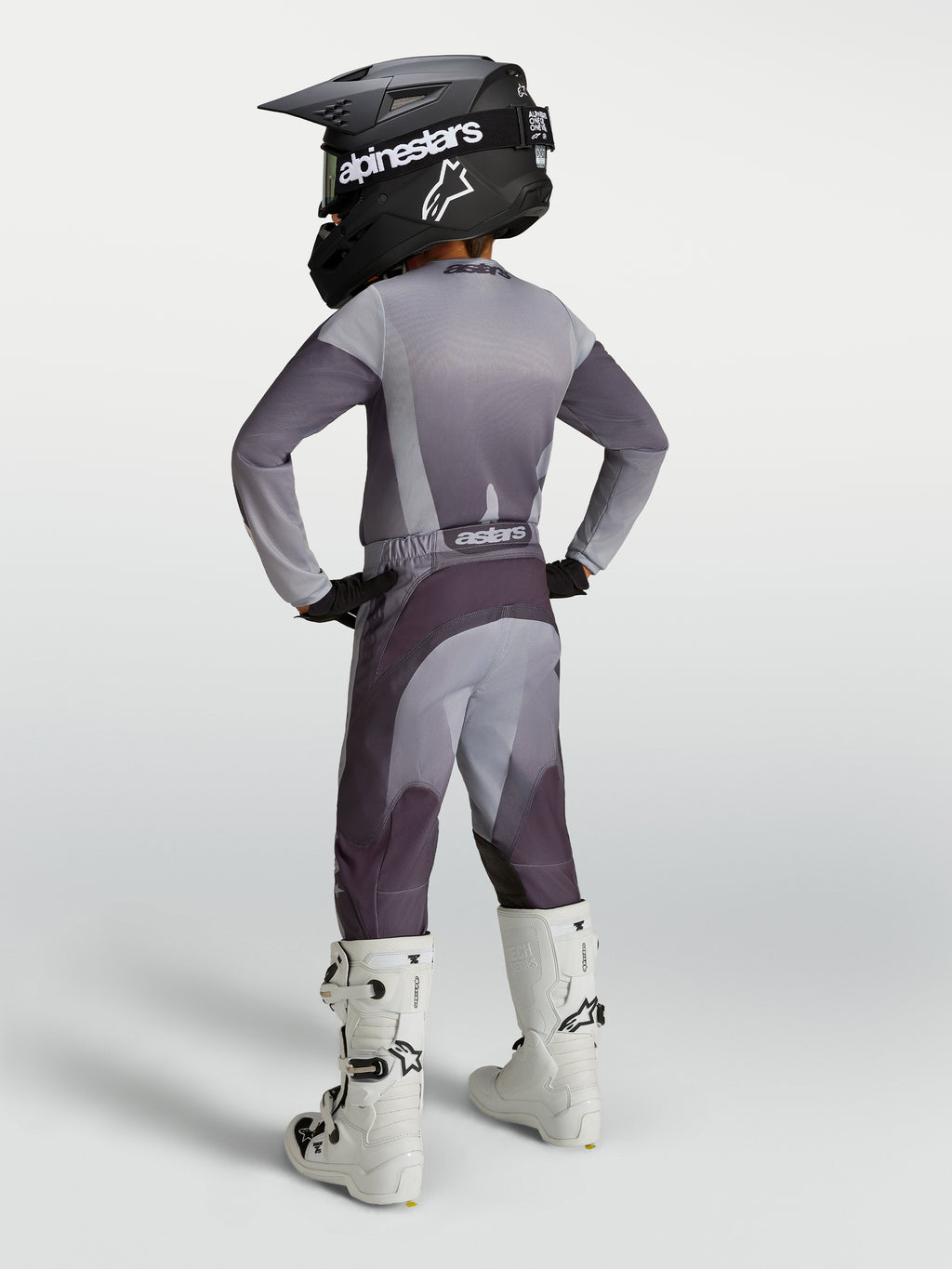 Alpinestars 2027 Jugend Fluid Amber Gear Set, Motocross-Outfit in Grau und Lila, Rückansicht mit Helm und weißen Stiefeln.