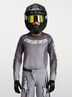 Alpinestars Fluid Jugend-Trikot Amber 2027, atmungsaktives Motocross-Trikot für Offroad, Grau und Sand, getragen mit Helm.