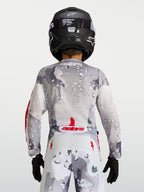 Alpinestars Fluid Jugend-Trikot Lone 2027, graues Camo-Motocross-Trikot, Rückansicht mit roten Akzenten und schwarzem Helm.