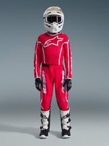 Young motocross rider wearing Alpinestars 2026 Youth Fluid Apex Jersey in Red and White, matching red pants with white logos, white helmet with goggles, white and black boots, and black and white gloves, complete coordinated gear for off-road racing