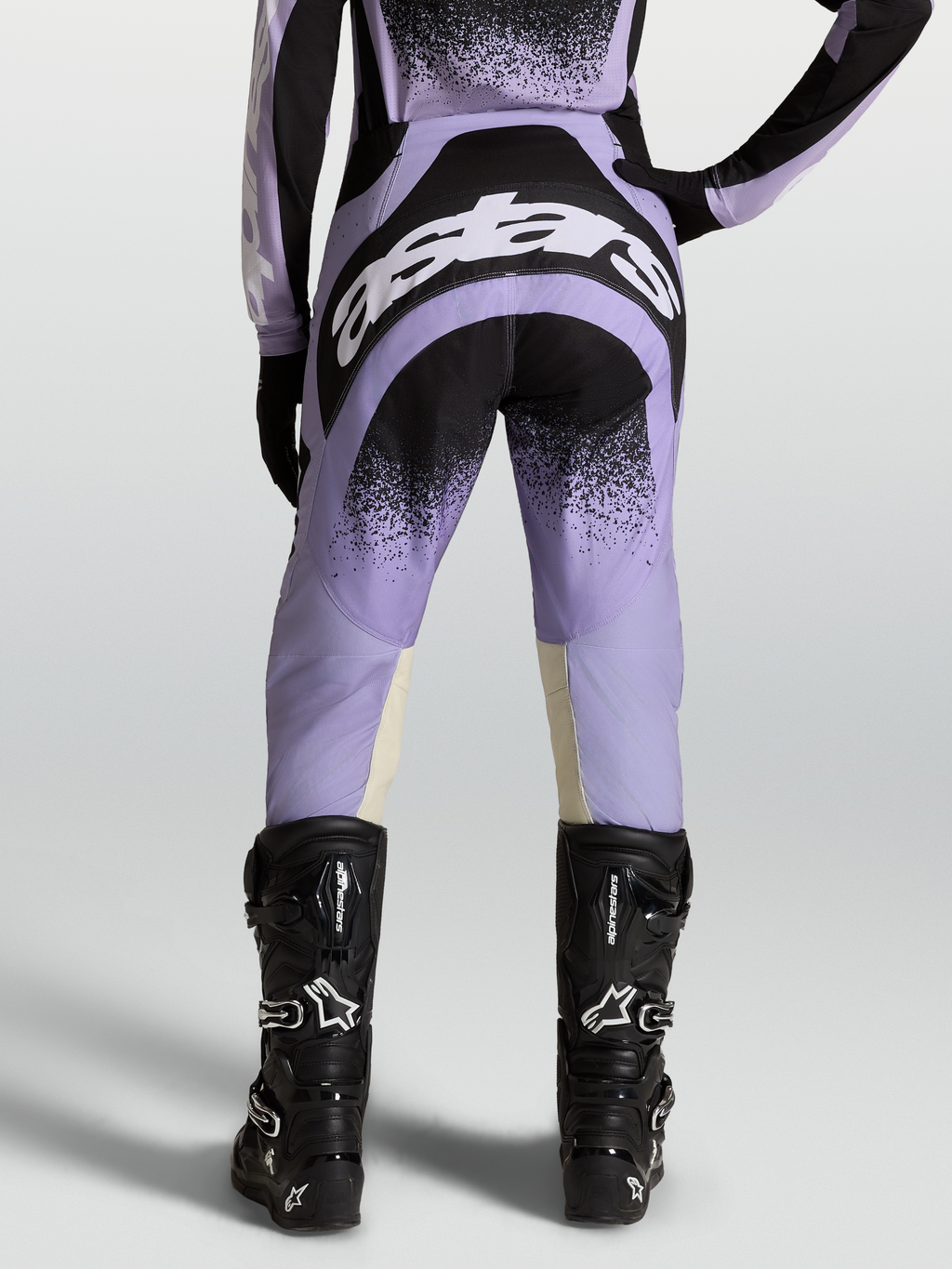 Alpinestars Stella Techstar Hose Swan, Damen-Motocross-Ausrüstung in Lila und Schwarz mit weißen Logos, getragen von einem Model mit schwarzen Stiefeln.