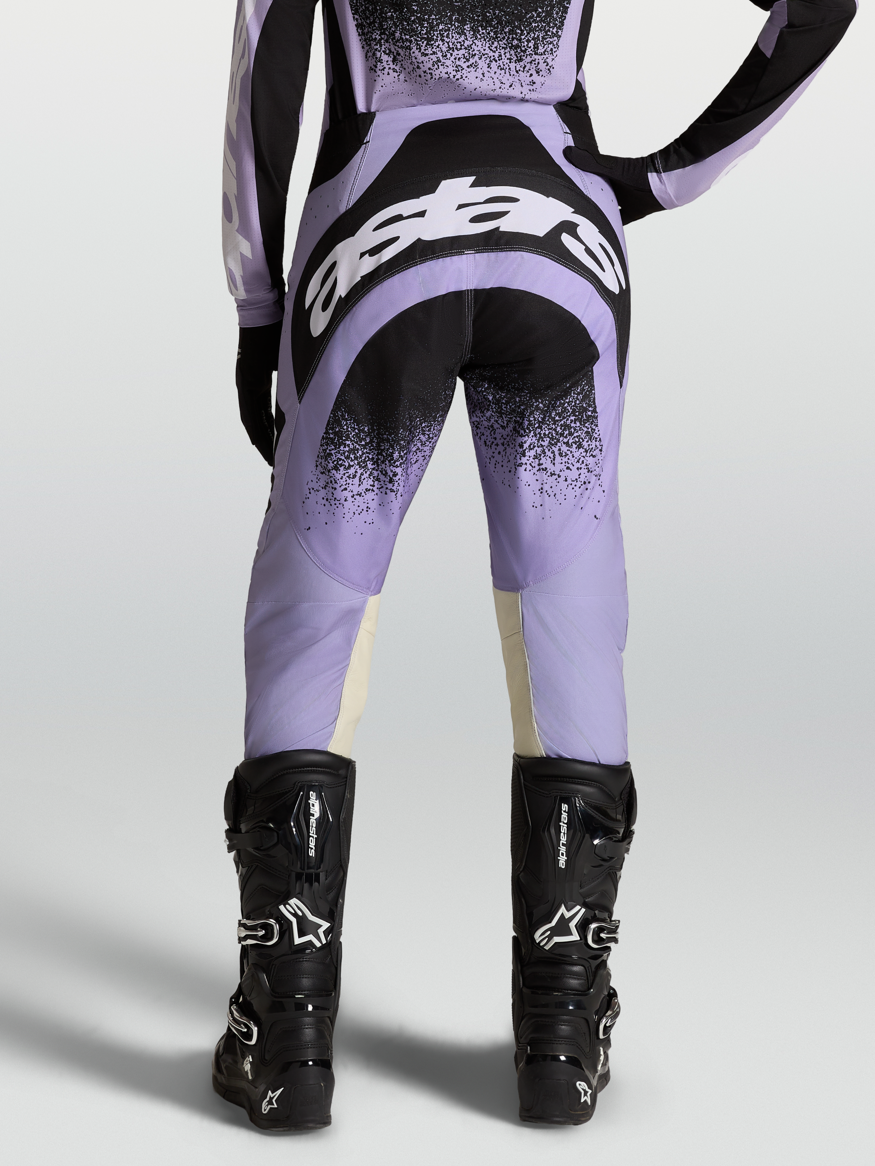 Alpinestars Stella Techstar Hose Swan, Damen-Motocross-Ausrüstung in Lila und Schwarz mit weißen Logos, getragen von einem Model mit schwarzen Stiefeln.