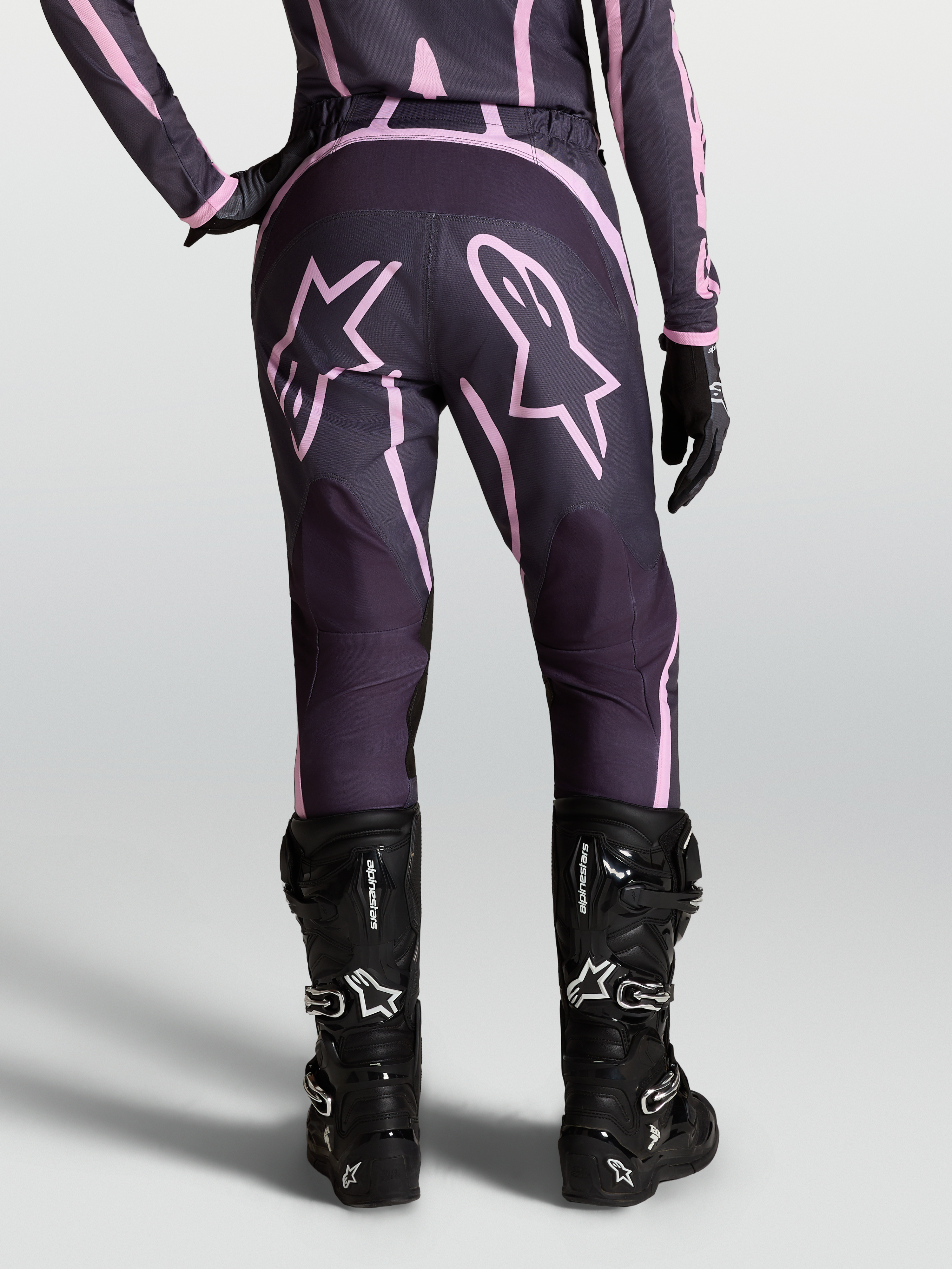 Alpinestars Stella Fluid Apex V2 Hose, Damen-Motocross-Hose in Grau und Pink, mit Sterngrafiken am Gesäß und schwarzen MX-Stiefeln, Rückansicht am Model.