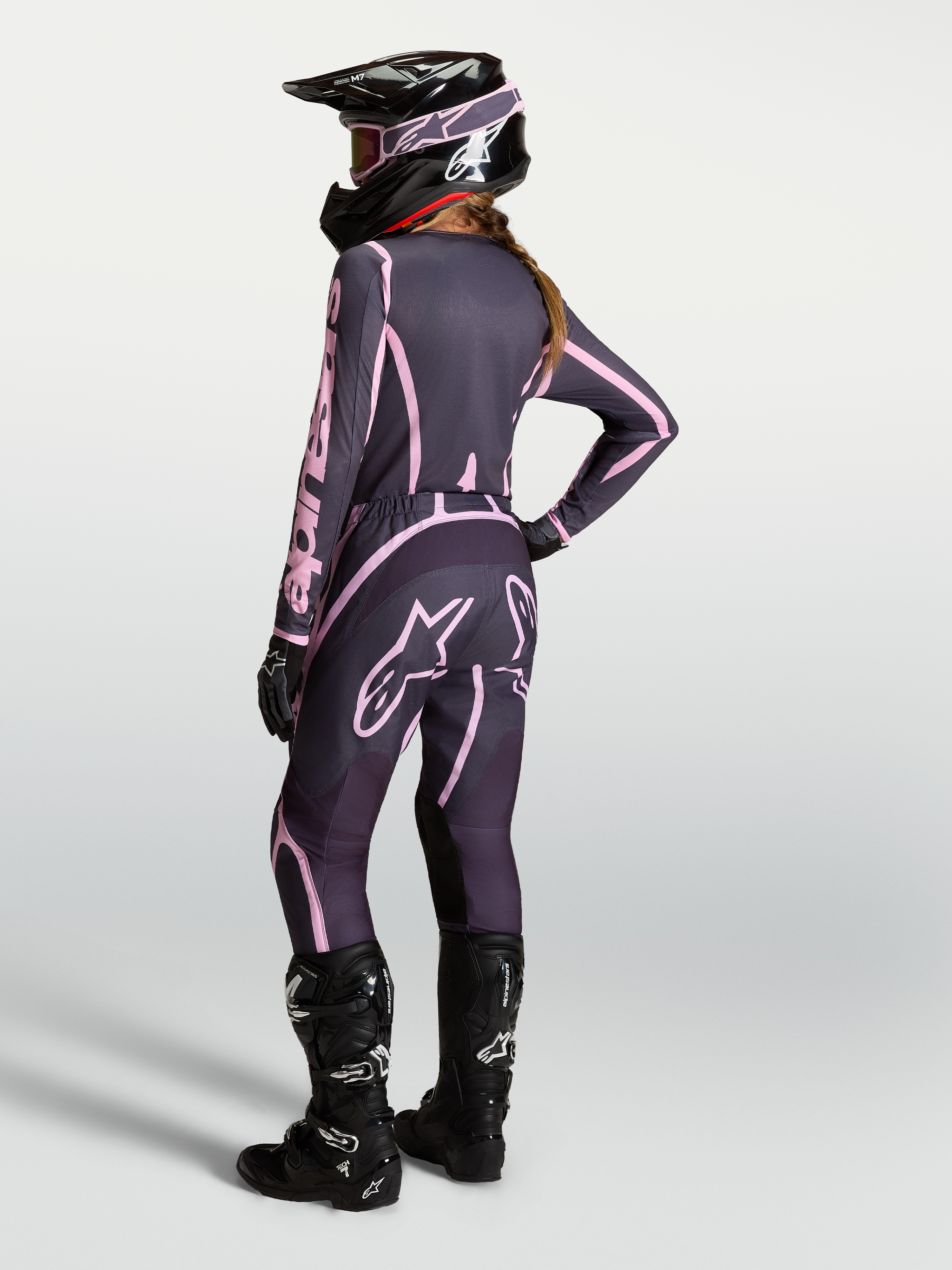Alpinestars Stella Fluid Apex V2 Hose, Motocross-Hose für Damen in Grau und Pink, Rückansicht einer kompletten Offroad-Ausrüstung mit Trikot, Tech 7 Stiefeln und Helm.