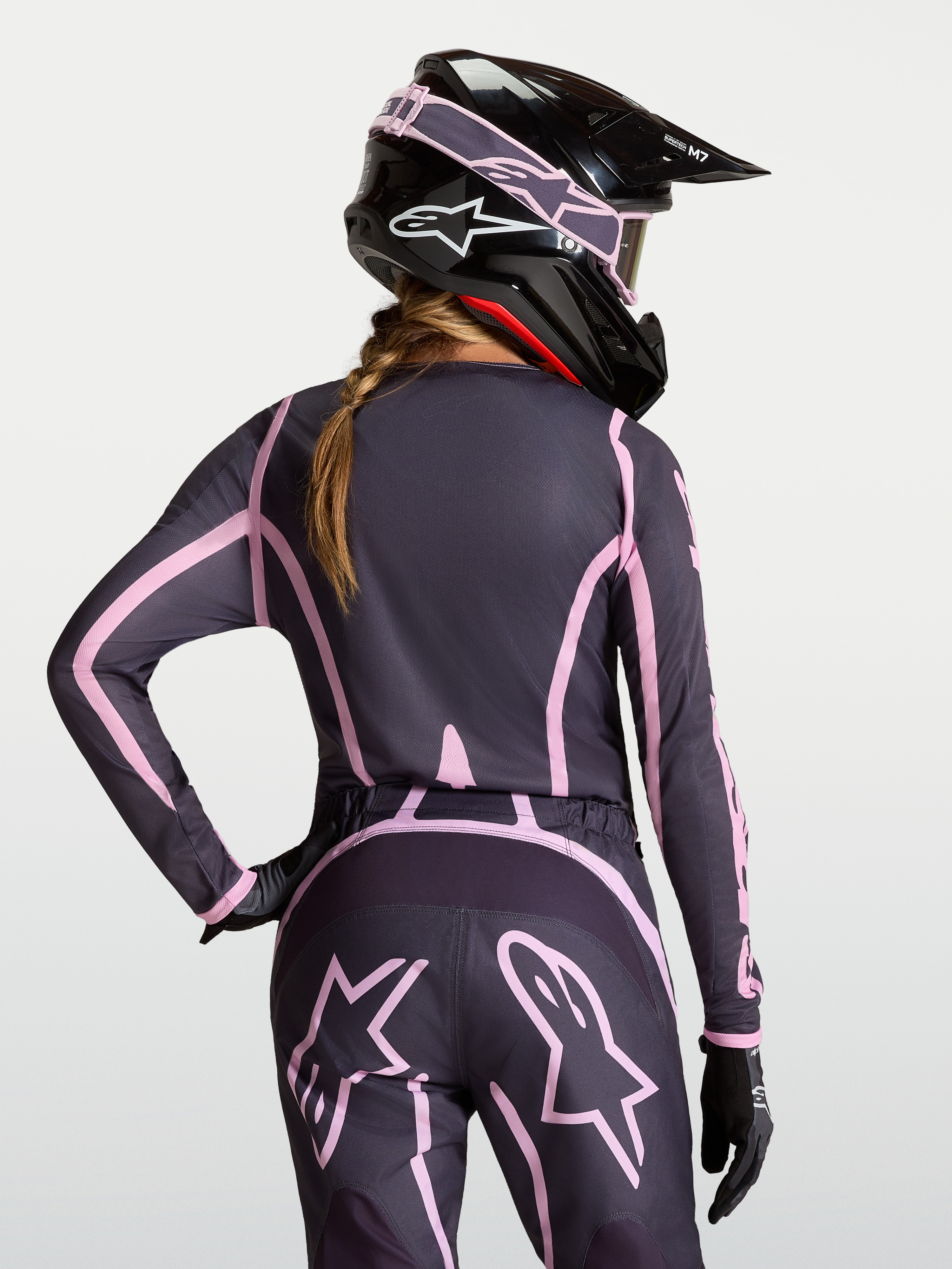 Alpinestars Stella Fluid Apex V2 Trikot, Damen-Motocross-Jersey in Grau und Rosa mit verlängerter Rückenpartie, am Modell getragen mit passendem Helm