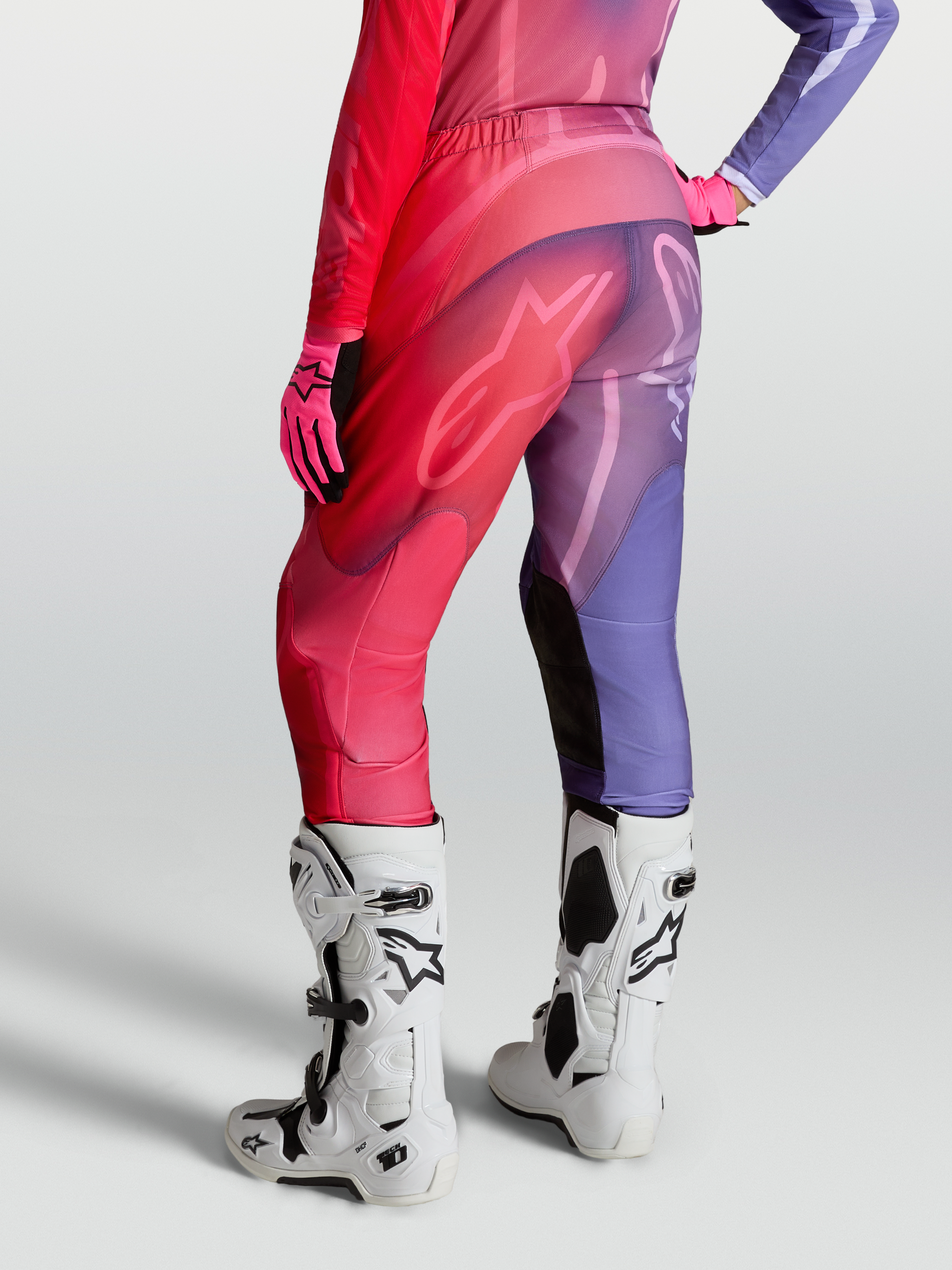 Alpinestars Stella Fluid Kepler Hose, Damen-Motocross-Hose in Lila und Rot, speziell vorgekrümmte Beine mit Stretch-Paneelen, Rückansicht mit Tech-10 Stiefeln und Handschuhen kombiniert.