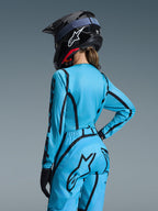 Alpinestars 2026 Stella Fluid Apex Bekleidungsset für Damen, Hellblau mit schwarzen geschwungenen Grafiken, Rückansicht an einer Fahrerin, getragen mit schwarzem Helm und Handschuhen, ergonomische Motocross-Bekleidung für Damen