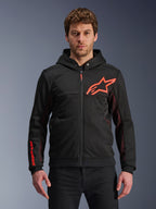 Alpinestars Chrome Air Sport Hoodie, schwarze Kapuzenjacke mit Reißverschluss, rotes Fluo-Stern-Logo und Akzente an den Ärmeln, rote Mesh-Seitenpaneele zur Belüftung, lässige urbane Motorradbekleidung, getragen von einem Model