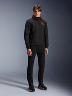 Alpinestars MM93 Radium Tech Hoodie, urbane Motorradjacke, Schwarz mit leuchtend roten Akzenten, getragen von einem Model mit schwarzer Hose und Motorradschuhen, mit rotem „93“-Logo auf der Brust und Marc Marquez Branding am Ärmel, lässige technische Streetwear für die Stadt
