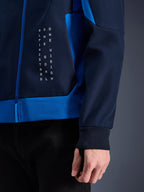 Alpinestars Radium Tech Hoodie, Urbaner Motorrad-Hoodie, Night Navy und Royal Blue, Nahaufnahme des Seitenteils mit weißer vertikaler Textgrafik, geripptem Stretch-Bündchen und blauem Reißverschluss