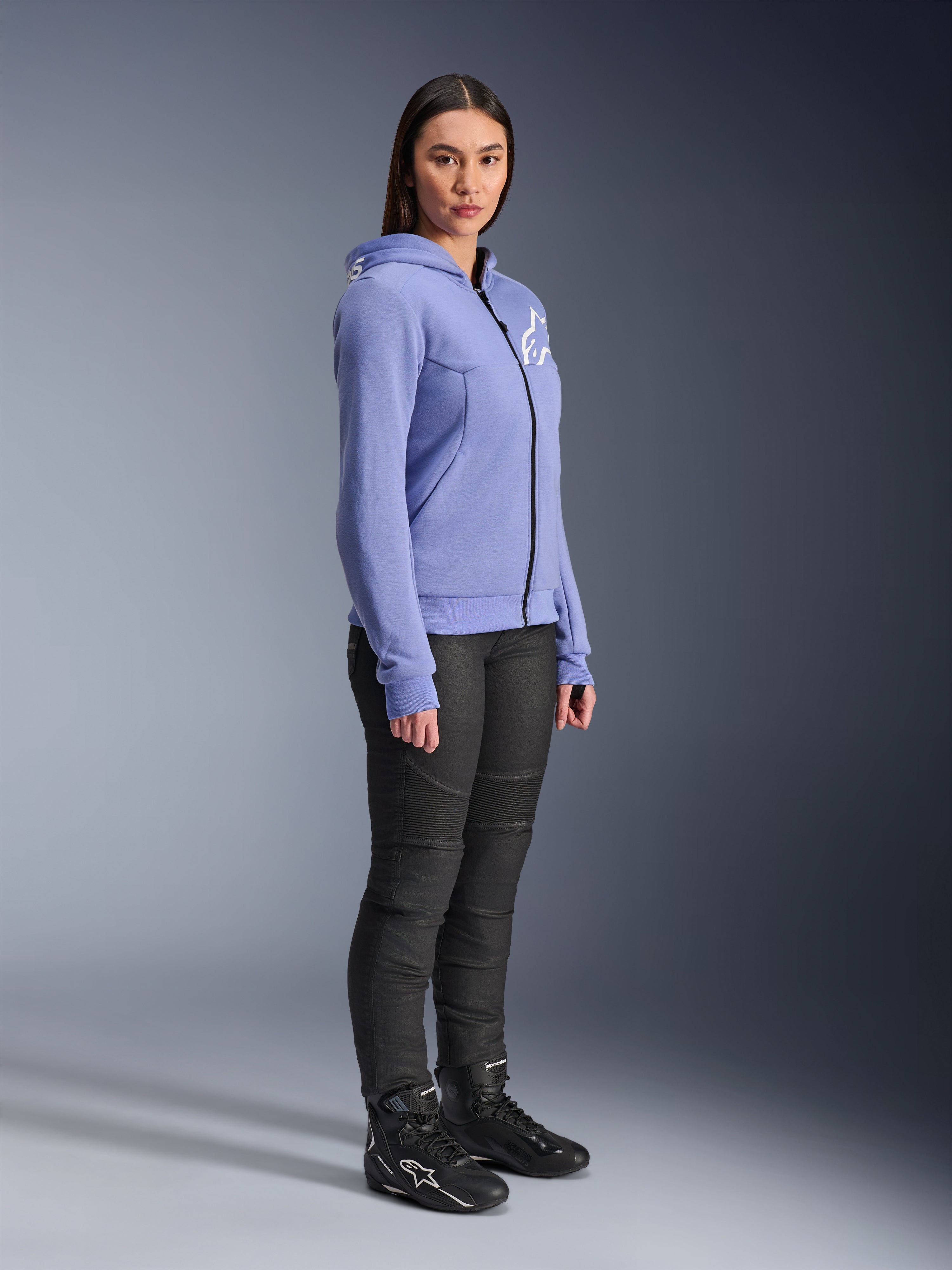 Alpinestars Woman Stella Chrome V2 Sport Hoodie, motorcycle hoodie in blue-violet with white Alpinestars logo on the chest, worn by a model with black riding pants and black motorcycle boots, urban riding apparel for women