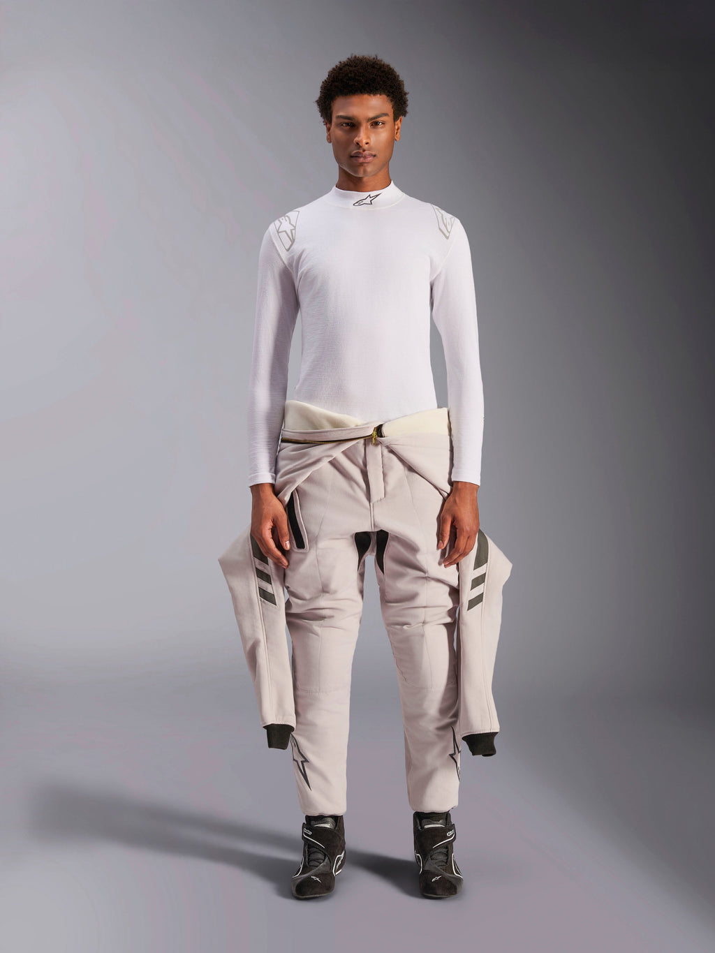 Alpinestars ZX Evo V3 Top, Langarm, Weiß, Auto-Rennsport-Basisschicht, getragen mit einem hellen Rennanzug um die Taille und schwarzen Rennstiefeln, mit Stehkragen mit Logo und Schulter-Branding, professionelle flammenresistente Motorsport-Unterwäsche