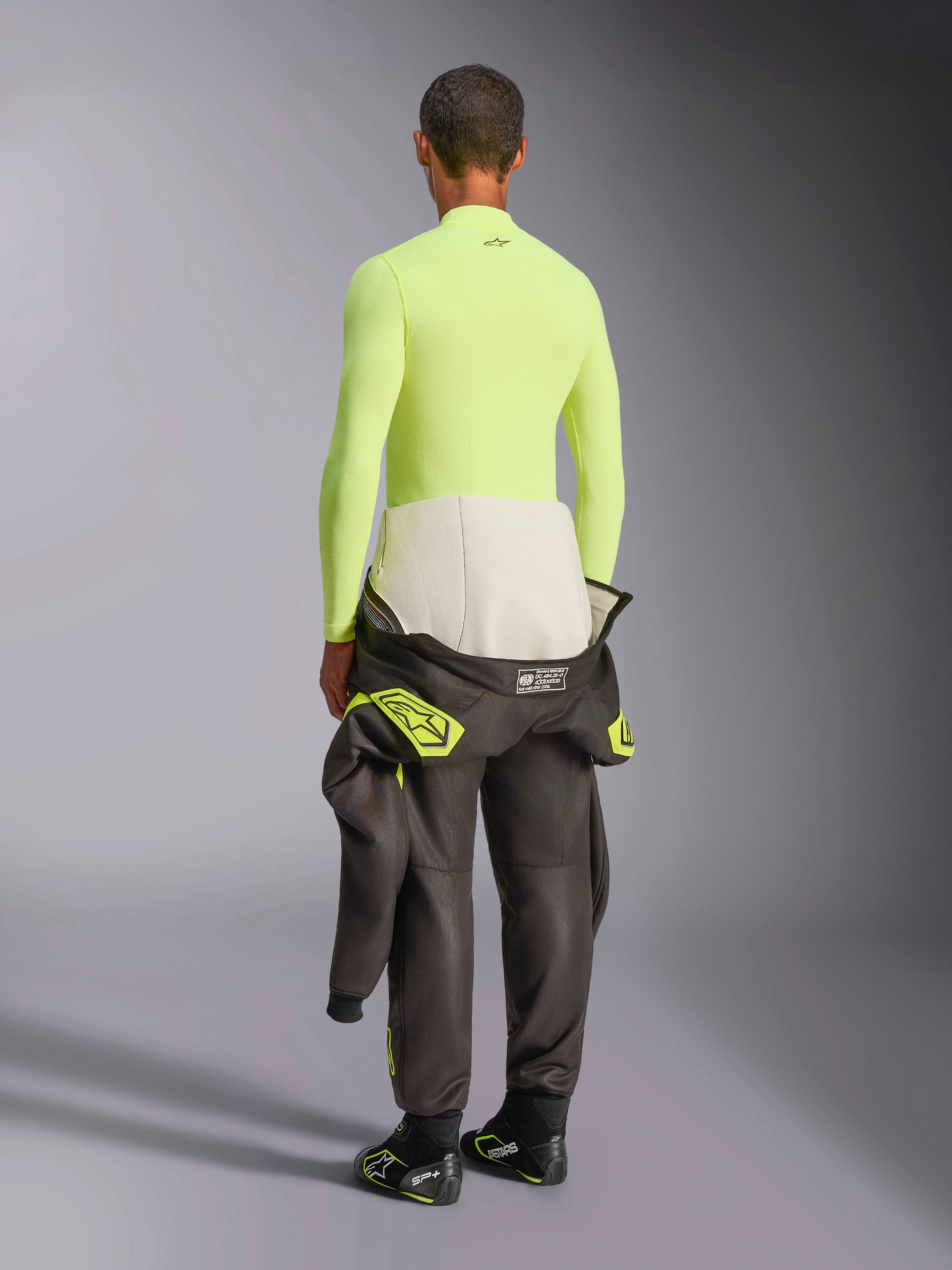 Alpinestars ZX Evo V3 Langarm-Oberteil, Yellow Fluo, Rückansicht eines Models in feuerfester Funktionsunterwäsche mit dunkler Rennanzughose und Stiefeln, professionelle technische Motorsport-Unterwäsche