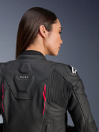 Woman wearing Alpinestars Stella Dusk Leather Jacket, black leather with Diva Pink accents and white logo on shoulder, back view showing DUSK branding and accordion stretch panels, sporty ergonomic design