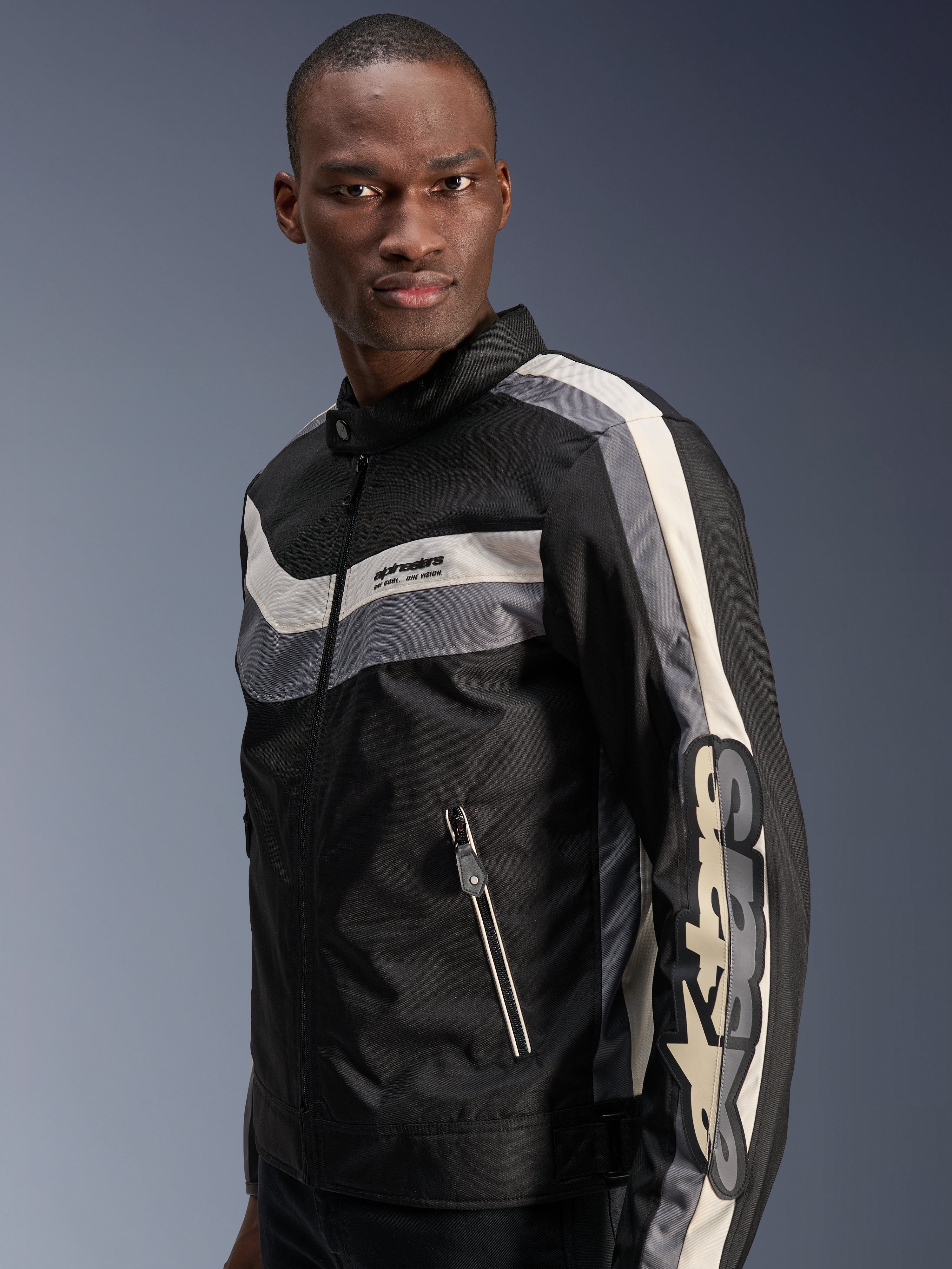 Alpinestars T-Dyno WR Jacke, Schwarz, Dunkelgrau und Ecru, vintage-inspirierte Textil-Motorradjacke mit horizontalen Bruststreifen, großem vertikalen Branding am Ärmel und Fronttaschen mit Reißverschluss, urbane Straßenausrüstung