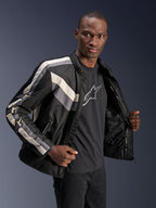 Alpinestars T-Dyno WR Jacke, Schwarz, Dunkelgrau und Ecru, Textil-Motorradjacke mit vintage-inspirierter Biker-Passform, Streifendetails auf Brust und Ärmeln, getragen über einem schwarzen Grafik-T-Shirt, urbane Fahrerausrüstung