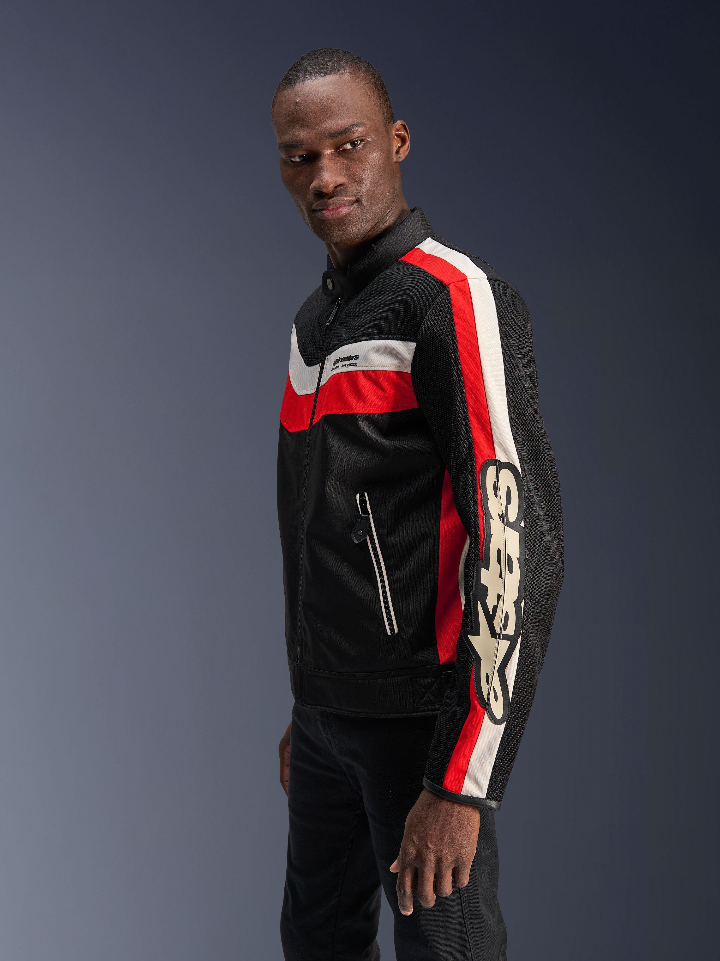Männliches Model in der Alpinestars T-Dyno Air Jacke in Schwarz, Bright Red und Ecru, Vintage-inspirierte Textil-Motorradjacke mit 3D-Mesh-Einsätzen, markanten roten und cremeweißen Streifen sowie auffälligem Alpinestars-Branding auf dem Ärmel.
