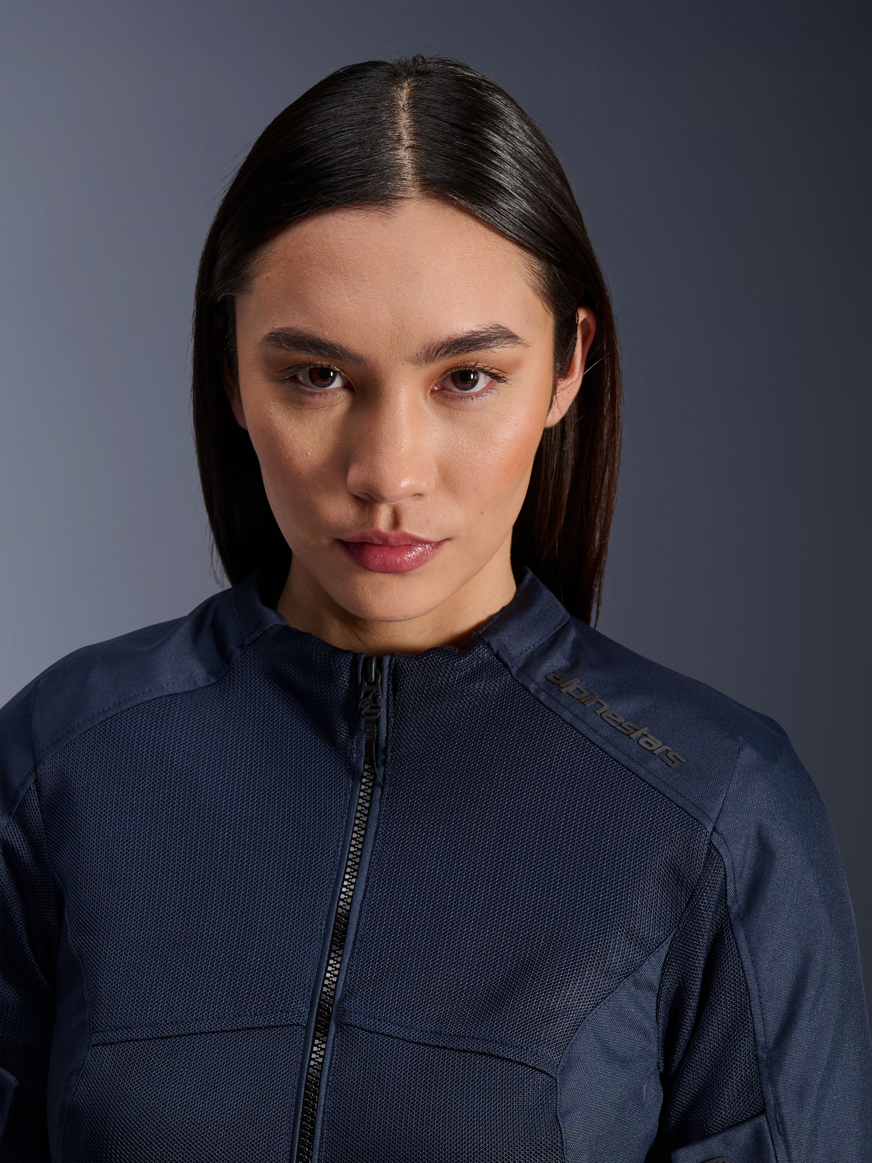Weibliches Model trägt die Alpinestars Stella C-1 Air Jacke in Dunkelblau, Nahaufnahme der atmungsaktiven Mesh-Textilstruktur, Reißverschluss vorne, Alpinestars-Logo am Kragen, elegante urbane Motorradbekleidung