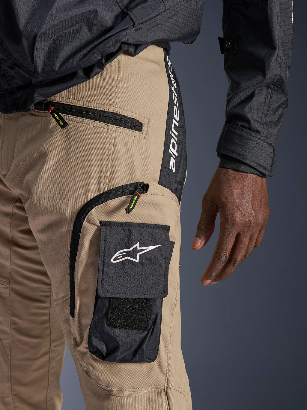 Alpinestars Acteon Hose in Sand, Detailansicht des Hüft- und Oberschenkelbereichs, schwarze seitliche Cargotasche mit weißem Stern-Logo, Reißverschlusstaschen, vertikales Alpinestars-Branding auf einem schwarzen Seitenpanel, urbane Motorradbekleidung