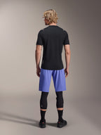Alpinestars A-Aria Switch Kurzarmtrikot, schwarzes MTB-Trikot, Rückansicht, kombiniert mit blauen Mountainbike-Shorts und schwarzem Beinschutz, Performance-Fahrradausrüstung für Trailfahrten