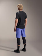 Männliches Model in der Rückansicht trägt Alpinestars A-Aria Lite Shorts in Baja Blue, kombiniert mit einem schwarzen Kurzarmtrikot und schwarzen Knieprotektoren, professionelle MTB-Radsportbekleidung für Trail-Riding.