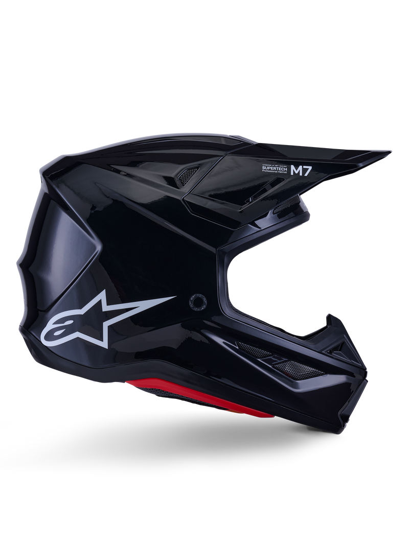 Alpinestars S-M7 Solid Helmet, Motocross Racing Helmet, Glossy Black with White Star Logo and Red Accents, side profile featuring aerodynamic design with angular mesh vents and Supertech M7 branding on the visor.