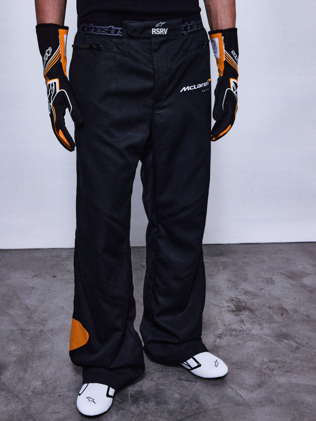 RSRV Arena Suit Pants, Schwarze Rennhose, McLaren und Alpinestars Logos, Orange Patches an der Seite, Orange Kniedetail, Motorsport-Performance-Hose