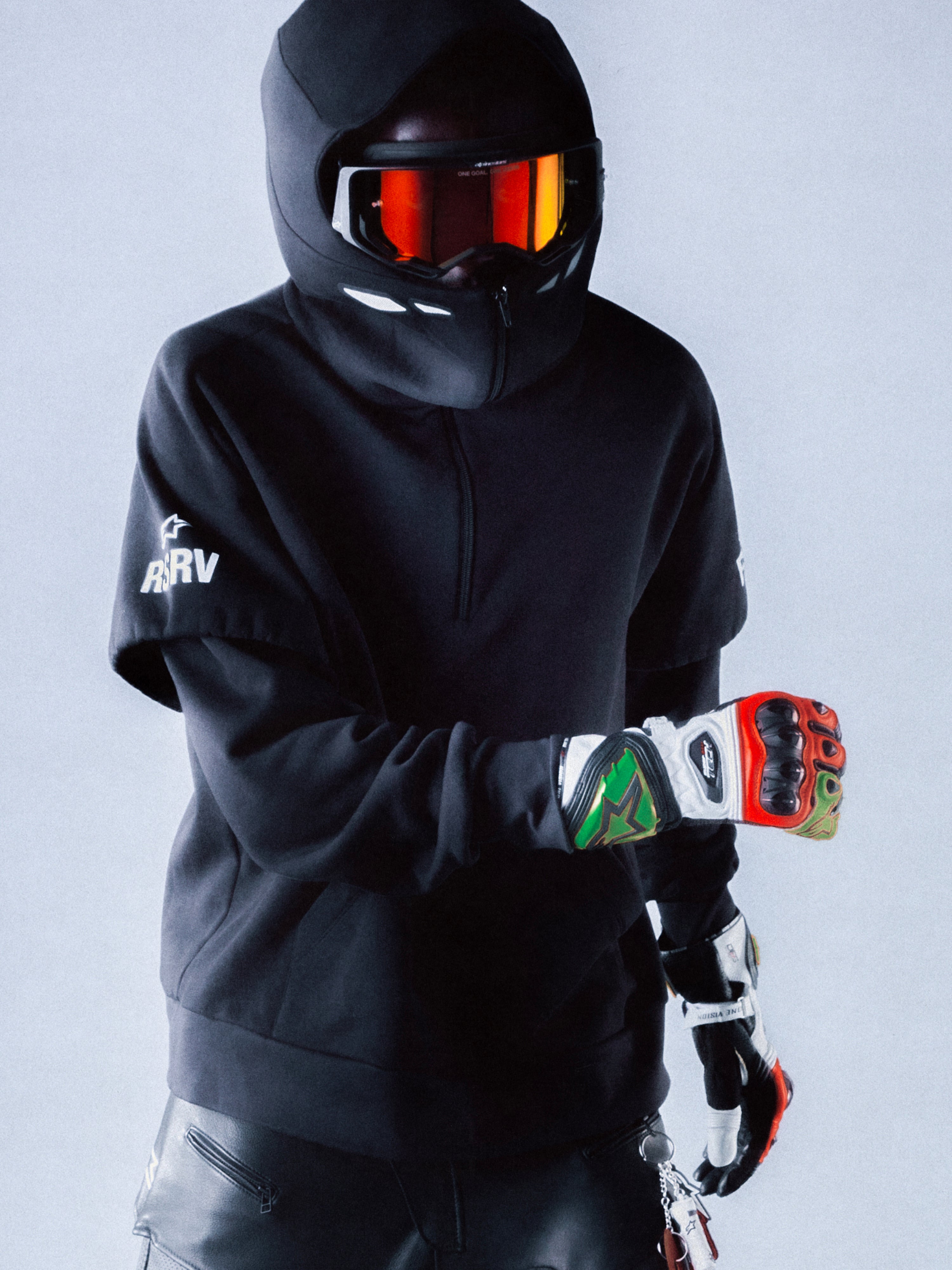 RSRV Vault Hoodie, Premium Streetwear Kapuzenpullover, Schwarz, Unisex, Motorsport-inspiriertes Design mit reflektierendem Logo, Person mit Helm und Handschuhen, urbaner Lifestyle-Look