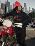 Alpinestars Pulse Hoodie, Black, hooded pullover fleece with red and grey Astars Combo Logo, worn by a man in an orange beanie standing next to a red Honda motorcycle in a city setting, casual motorsport streetwear