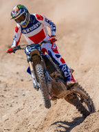 Motocross-Fahrer in Aktion auf einer Geländestrecke, trägt das Limited Edition Techstar Fortitude Trikot in Bright Red White and Blue, kombiniert mit farblich passender Rennhose und Stiefeln, mit markantem Alpinestars-Branding, professionelle Offroad-Rennbekleidung
