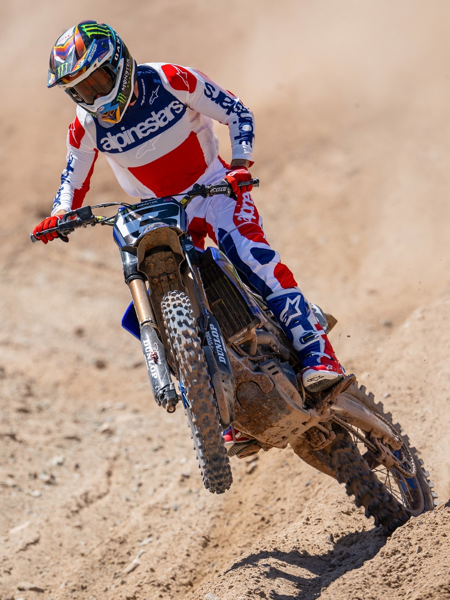 Motocross-Fahrer in Aktion mit Alpinestars Limited Edition Fortitude Tech 10 Stiefeln, Renn-Trikot und -Hose in hellem Rot, Weiß und Blau, abgestimmtes patriotisches Ausrüstungsset für Offroad-Performance auf einer Erdpiste