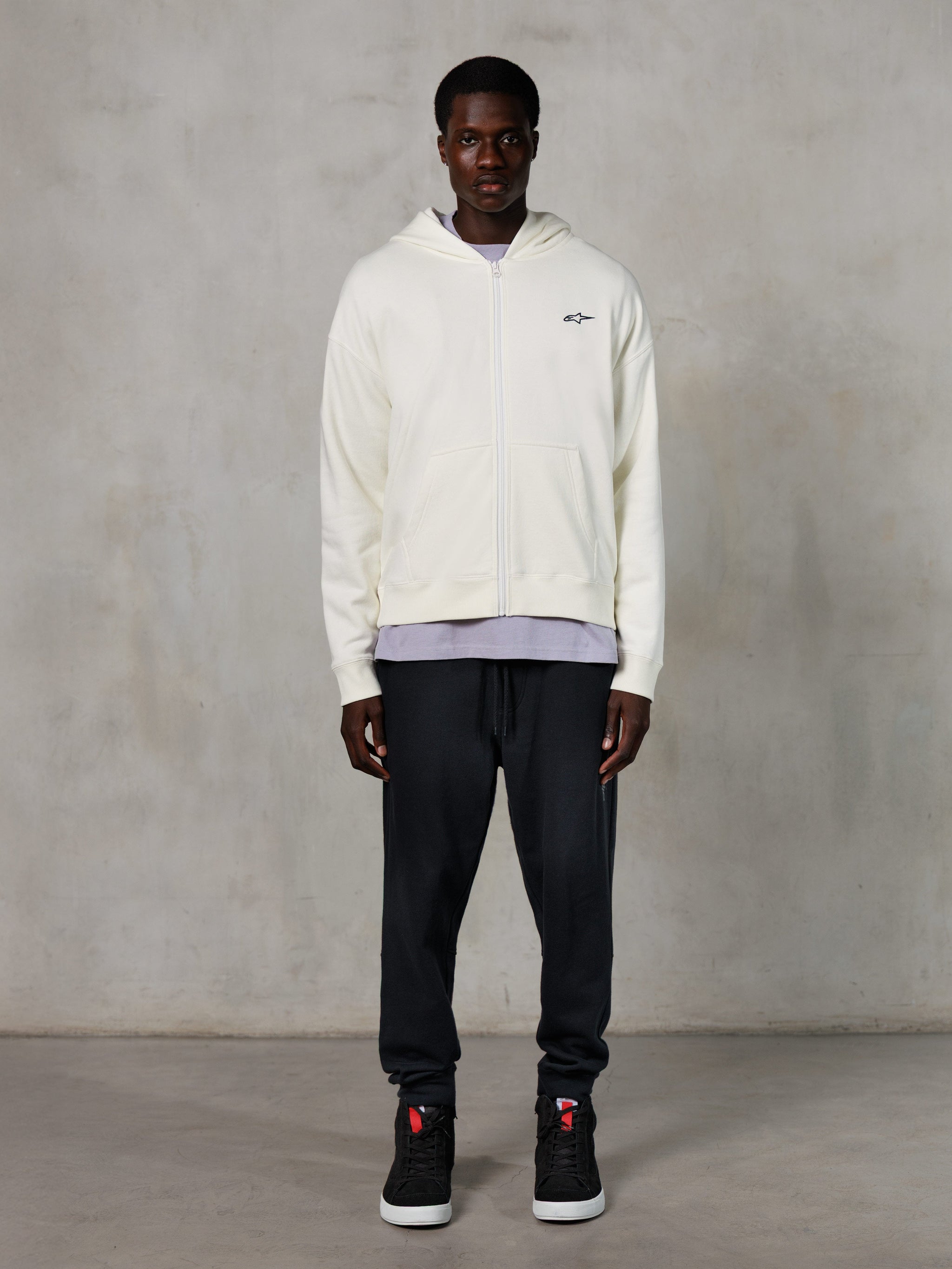 Alpinestars Essentials Ageless Zip Hoodie, lässige Streetwear, Off-White mit dezentem schwarzem Logo auf der Brust, durchgehender Reißverschluss vorne, Kapuzendesign, entspannte Passform, kombiniert mit schwarzer Jogginghose und Sneakern