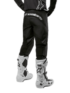 Alpinestars 2024 Fluid Graphite Ausrüstungsset, Rückansicht der schwarz-grauen Motocross-Hose mit weißem Alpinestars-Branding am Gesäß, weiße und schwarze Motocross-Stiefel, spezialisierte Offroad-Rennausrüstung