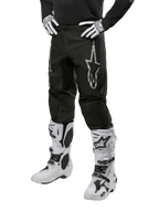 Alpinestars 2024 Fluid Graphite Hose, Motocross-Hose, Grau und Schwarz, kombiniert mit weiß-schwarzen Motocross-Stiefeln und Handschuhen, mit großem silbernen Alpinestars-Logo am Oberschenkel, sportlich-athletische Passform für Offroad-Fahrten