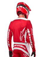 Motocross-Fahrer im Alpinestars 2024 Fluid Lurv Trikot, Mars Rot und Weiß, Rückansicht mit weißem Alpinestars-Logo auf dem Rücken und Branding an den Ärmeln, kombiniert mit einem passenden roten Helm und schwarzen Handschuhen, professionelle Offroad-Rennausrüstung