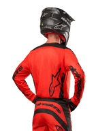 Motocross-Fahrer von hinten im Alpinestars 2024 Fluid Lurv Trikot in Hot Orange und Schwarz, mit auffälligem Alpinestars-Branding auf dem Rücken und den Ärmeln, kombiniert mit passender Motocross-Hose und einem schwarzen Helm, entwickelt für Offroad-Rennsport-Performance.