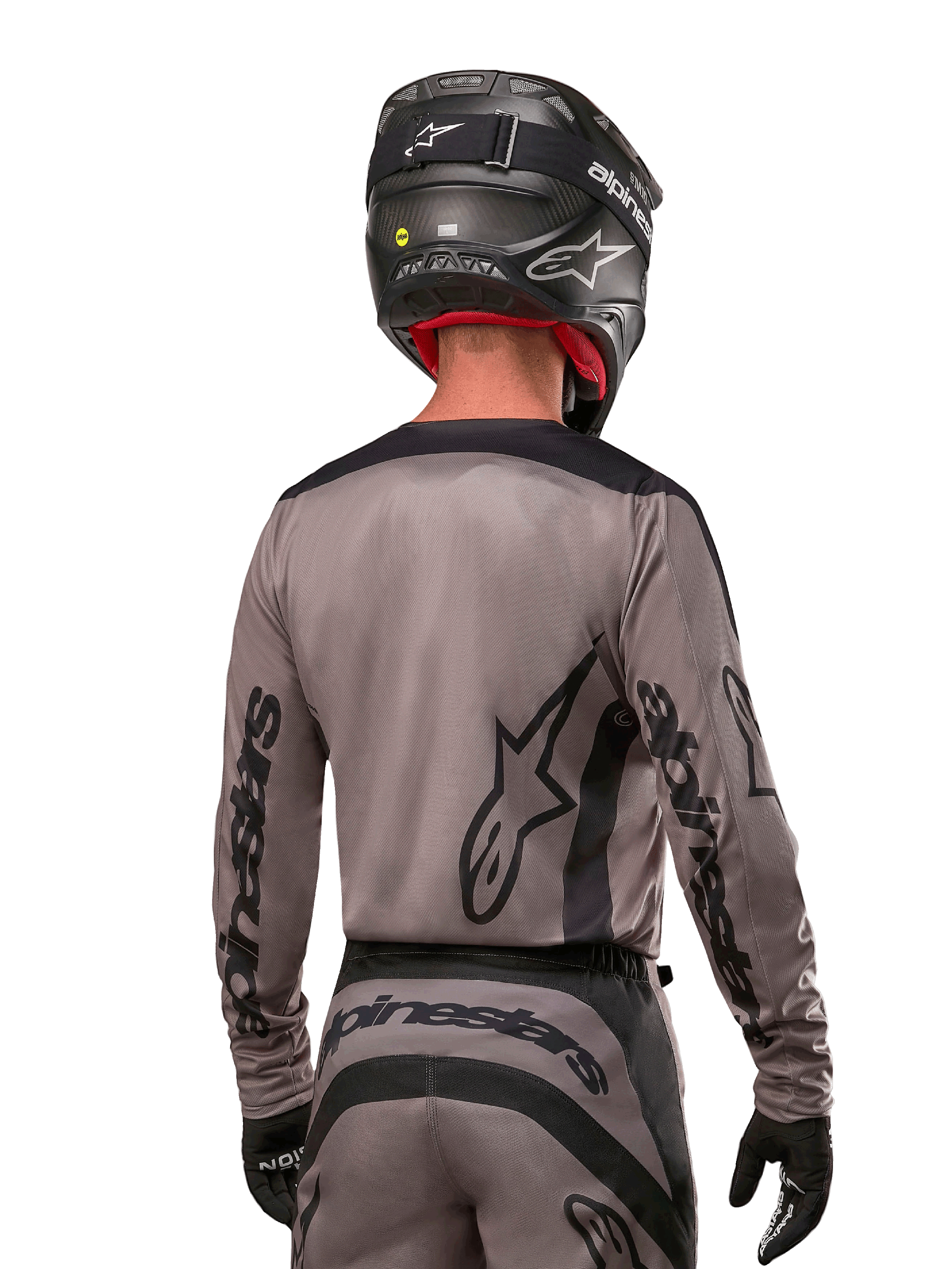 Motocross-Fahrer in der Rückansicht, trägt das Alpinestars 2024 Fluid Lurv Trikot in Mud Black, mit schwarzem Alpinestars-Branding auf Ärmeln und Rücken, kombiniert mit einem schwarzen Helm und passender Ausrüstung für den Offroad-Rennsport