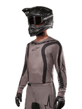 Alpinestars 2024 Fluid Lurv Trikot, Motocross-Jersey, Mud Black und Grau, langärmliges Design mit geschwungenen schwarzen Streifen und Logos, getragen mit passender Hose und einem schwarzen Motocross-Helm, abgestimmte Offroad-Rennausrüstung