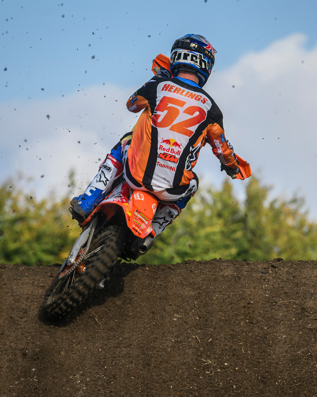 Motocross rider Jeffrey Herlings in action on a dirt track with a clear blue sky.
